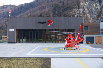 Detailansicht der Rega-Basis Mollis mit dem rot-weissen Rettungshelikopter AW109 SP Da Vinci (HB-ZRZ) auf der Landefläche vor dem Hangar.