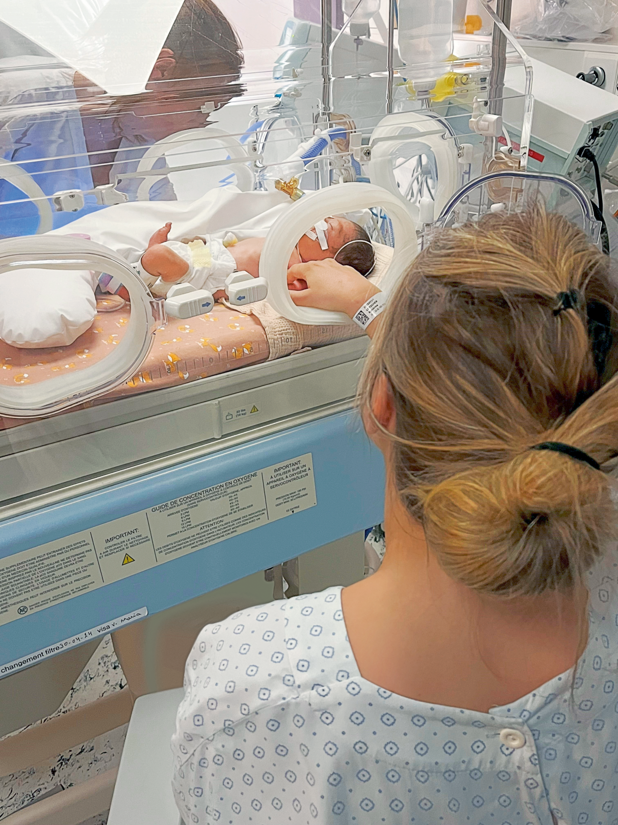 Une personne regarde un bébé allongé dans un incubateur.