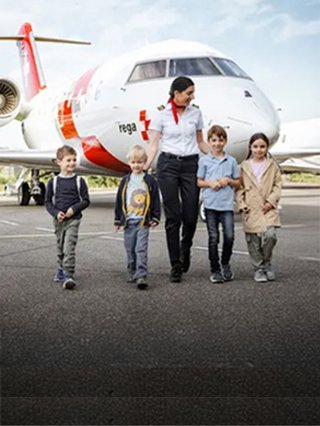 A Rega employee walks with a group of children on the tarmac, passing an ambulance jet.