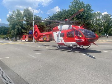 Un hélicoptère de sauvetage Rega rouge et blanc atterrit sur une route près du CERN à Genève. D'autres véhicules d'intervention sont visibles en arrière-plan.
