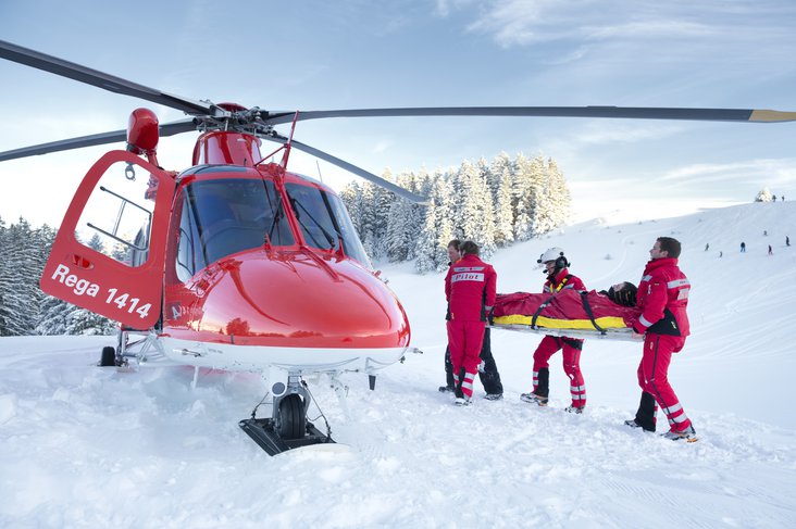 Die Rega-Crew trägt mit Hilfe des Pistenpatrouilleurs einen verletzten Wintersportler zum Helikopter.