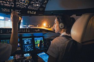 Daniela Bergamin, pilota di jet, seduta nella cabina di pilotaggio di un jet Rega di notte, concentrata sugli strumenti e un tablet.
