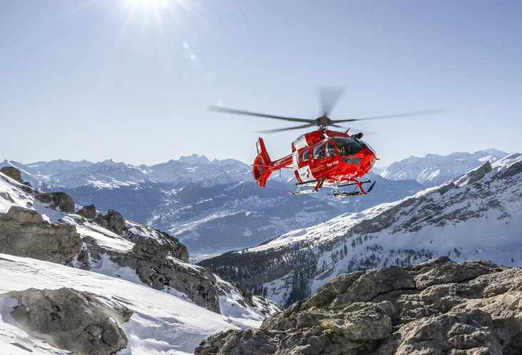 The Rega helicopter flies over the snow-covered mountains of Switzerland