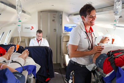 Rega flight nurse smiling while caring for patients on board an ambulance jet during a repatriation flight.