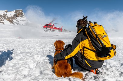 Lawinenhundeführer und sein Lawinenhund warten im Schnee bis der Rega-Helikopter gelandet ist