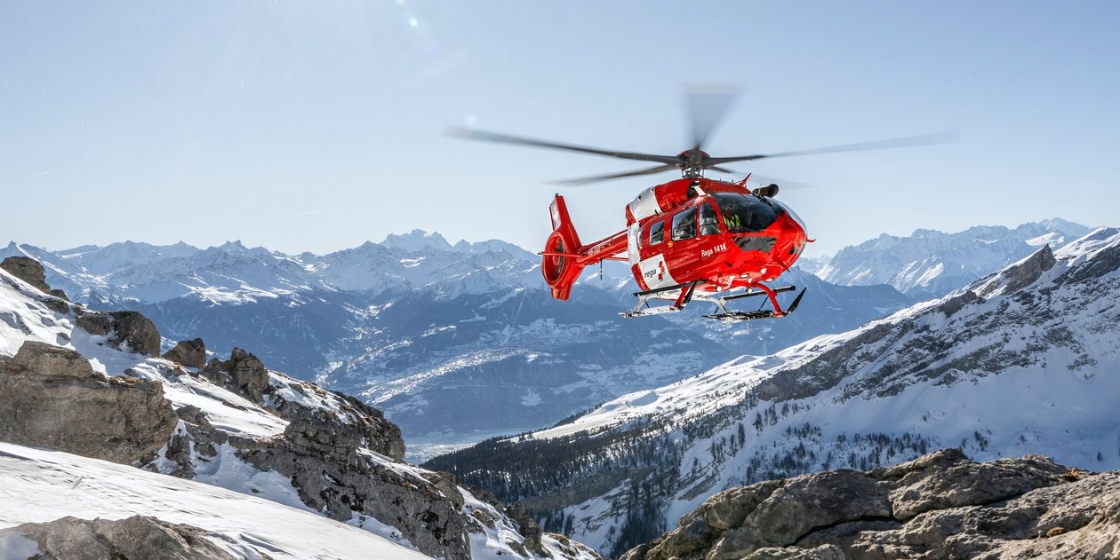 Un hélicoptère Rega survole les montagnes enneigées de Suisse