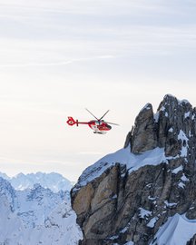 Rescue helicopter in flight in front of a boulder