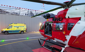 Un hélicoptère de la Rega se trouve sur l'héliport ; une ambulance est garée en face.