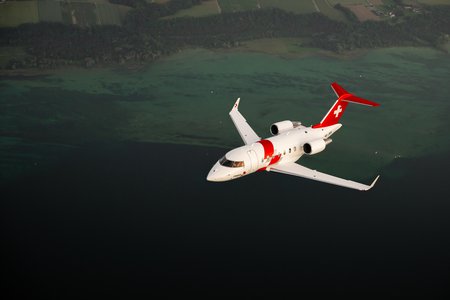 Zum Downloadformular für das Bild Rega-Ambulanzjet im Flug über einem See mit Uferlandschaft.