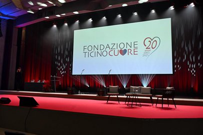 Un palco in un auditorium, allestito con poltrone per una tavola rotonda. Un grande schermo sullo sfondo mostra il logo della "Fondazione Ticino Cuore".