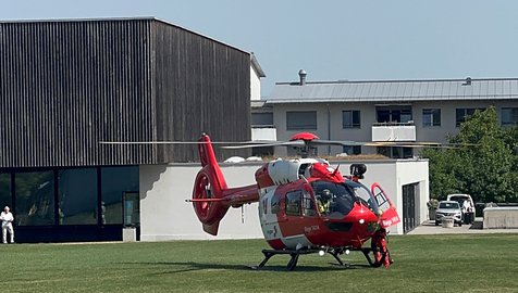 Un hélicoptère de sauvetage Rega Airbus H145 est posé sur une pelouse devant un bâtiment, avec sa porte ouverte.