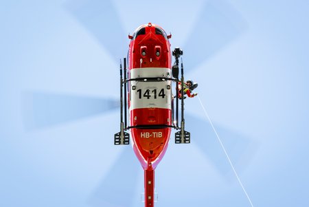 Zum Downloadformular für das Bild Rega-Helikopter von unten mit Rettungssanitäter beim Bedienen der Rettungswinde.