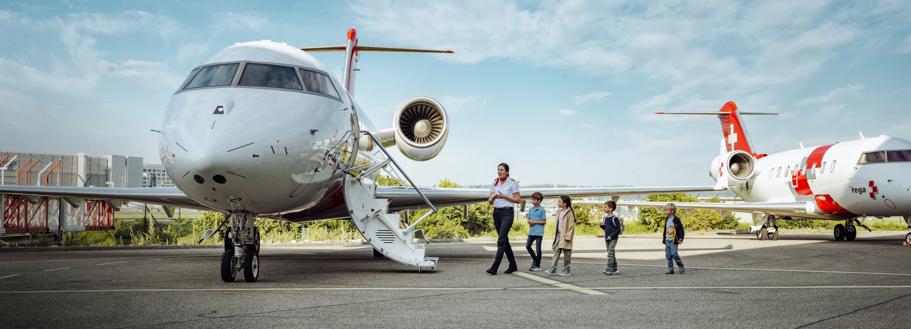 Une collaboratrice de la Rega se promène avec un groupe d'enfants sur le tarmac, passant devant un avion-ambulance.