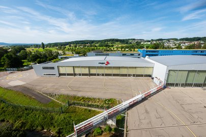 Vue extérieure du Centre Rega à l'aéroport de Zurich, avec les portes du hangar et la place d'atterrissage.