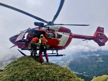Un hélicoptère de la Rega est posé sur un sommet de montagne herbeux.