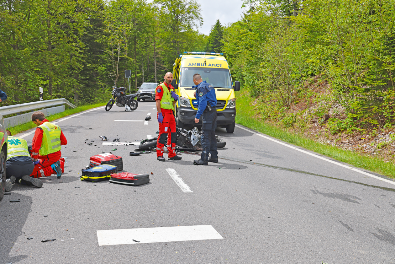 Les services d'urgence sont sur les lieux d'un accident de moto sur une route de campagne, avec une ambulance en arrière-plan.