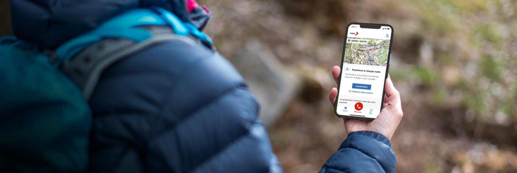 Una persona all'aperto tiene in mano uno smartphone con l'app Rega aperta, che mostra la posizione in tempo reale e l'opzione di chiamata d'emergenza.