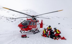 Rega crew treating a patient in the snow next to a rescue helicopter in the high mountains.