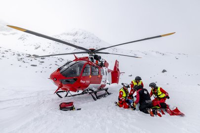 Rega crew treating a patient in the snow next to a rescue helicopter in the high mountains.