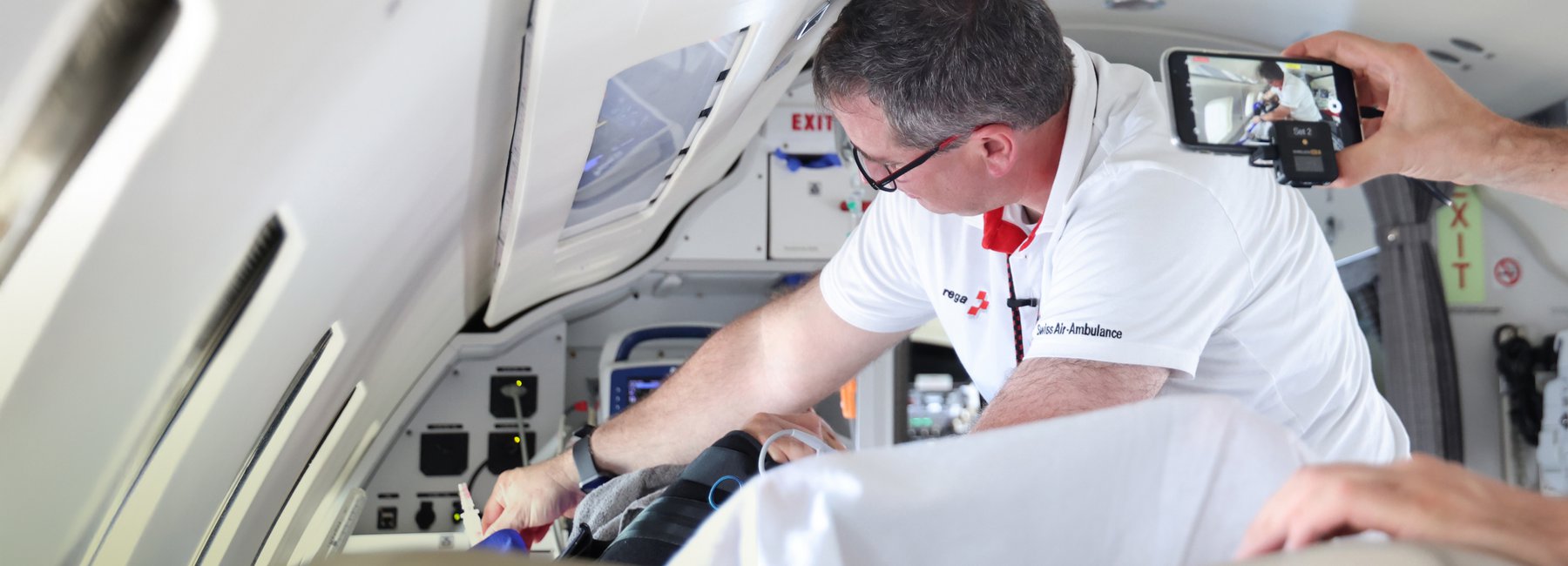 Une personne en tenue de la Rega filmée avec un smartphone alors qu'elle travaille à l'intérieur d'un avion-ambulance.