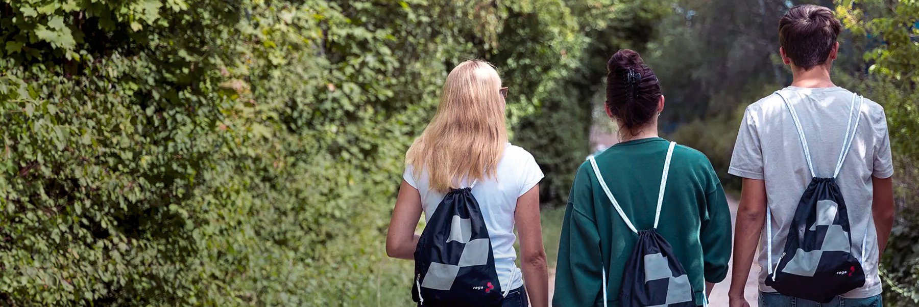 Drei Personen von hinten, die Rucksäcke tragen und durch einen Wald gehen.