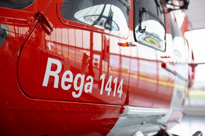 Gros plan d'un hélicoptère rouge de la Rega dans le hangar, avec l'inscription « Rega 1414 » bien visible.