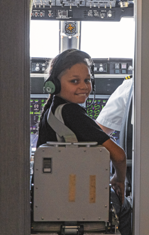 Ein Bub sitzt mit Kopfhörern im Cockpit-Bereich des Rega-Jets und lächelt in die Kamera. Im Vordergrund ist ein Patient auf einer Trage mit Überwachungsmonitor zu sehen.