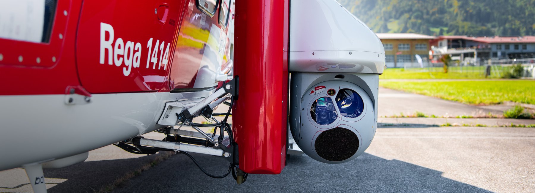 Close-up of a thermal imaging camera attached to a Rega helicopter. The text «Rega 1414» is visible on the helicopter.