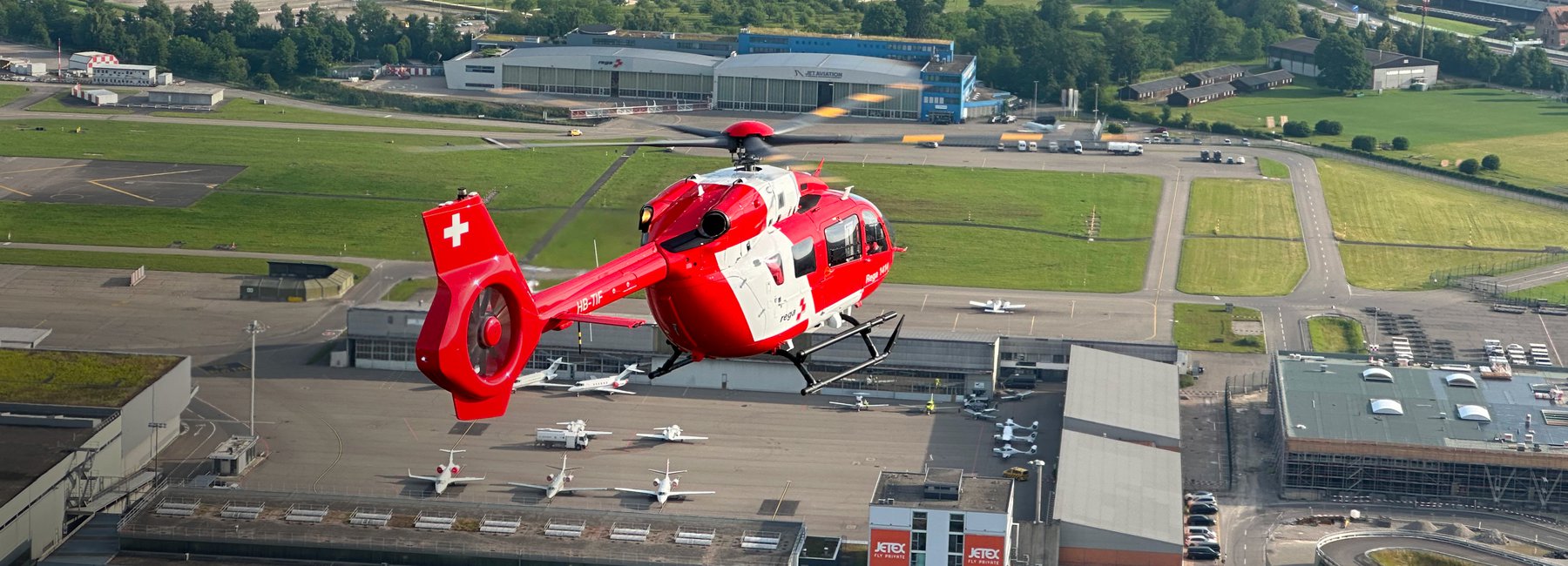 A Rega helicopter in flight above Zurich Airport.