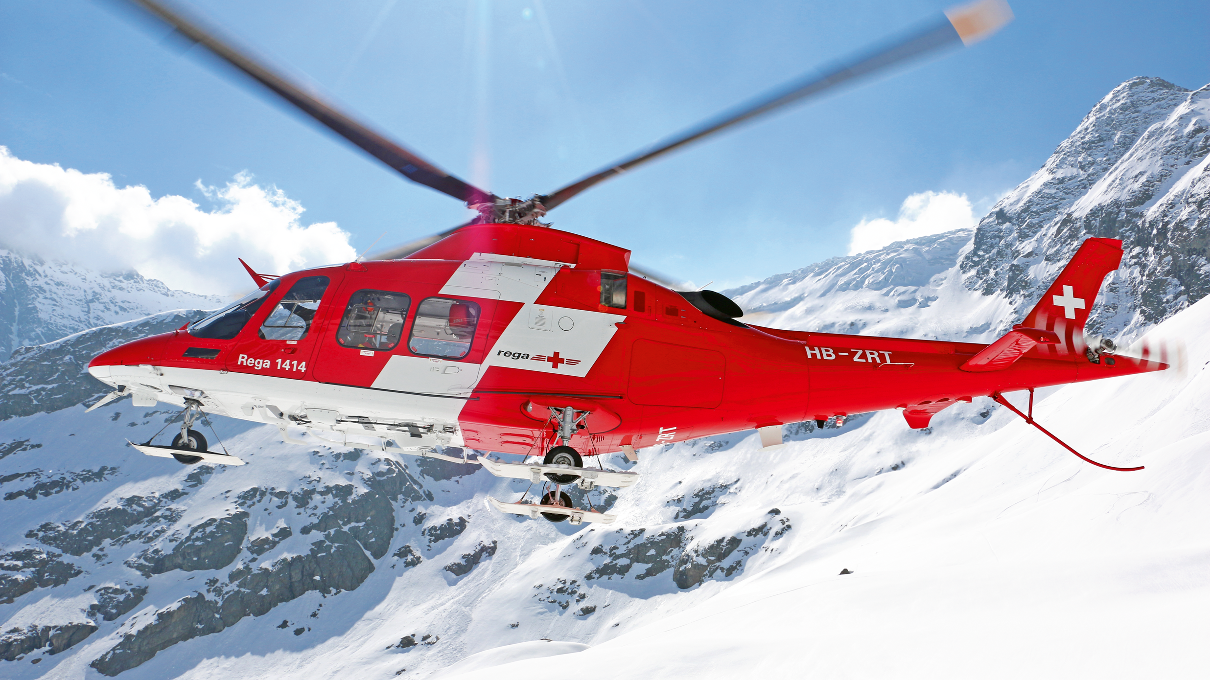 Elicottero rosso AgustaWestland Da Vinci in volo tra le montagne.